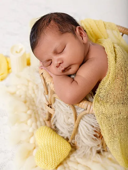 A close-up of a sleeping newborn in a basket, wrapped in a soft yellow blanket. The focus is on their serene and delicate features.