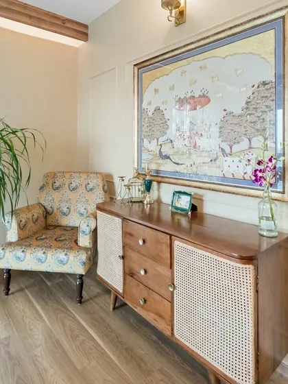 A cozy corner in the master bedroom, featuring a patterned armchair next to the wooden and rattan console. This vignette showcases a blend of traditional art, classic furniture, and comfortable design.