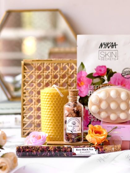 A beautiful flatlay of self-care products, including a beeswax candle, massage bar, and bath salts. The hexagonal mirror in the background adds a modern, geometric touch to the elegant arrangement.