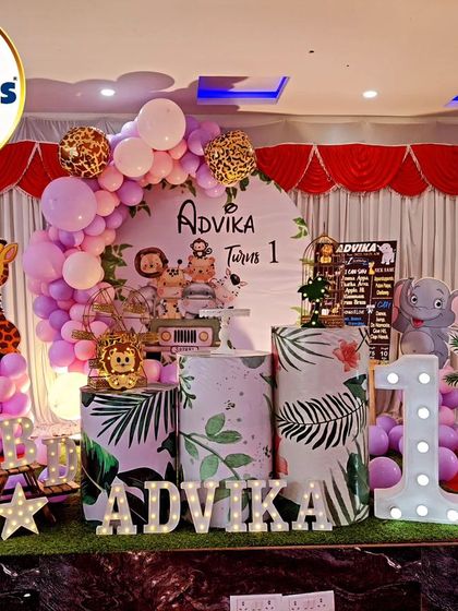 A jungle-themed first birthday with a soft purple and pink color scheme. The setup includes cutouts of a zebra, giraffe, and leopard, along with a large light-up number '1'.