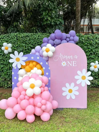 A sweet daisy-themed setup for Ariana's first birthday. This outdoor decor features a custom pink arch backdrop, a smaller arch filled with balloons, and cheerful daisy cutouts for a fresh, playful feel.