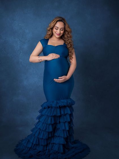 A classic solo portrait in a stunning royal blue ruffled gown, looking down at her bump with love.