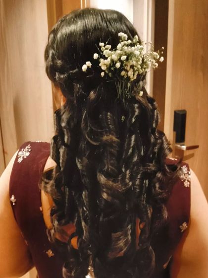A half-up hairstyle with tight curls and a baby's breath accessory. This look provides great volume and texture, perfect for a Sangeet or engagement.