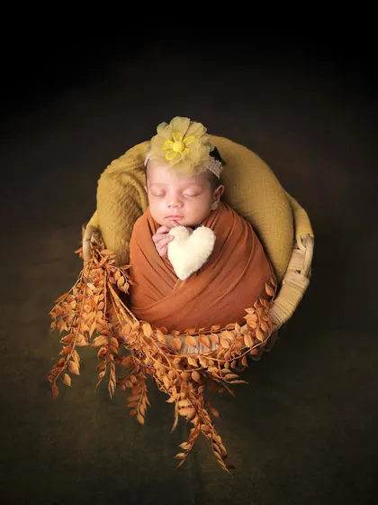 An earthy and warm newborn portrait. The baby is nestled in a basket with autumn leaves, holding a small heart, creating a cozy and loving image.