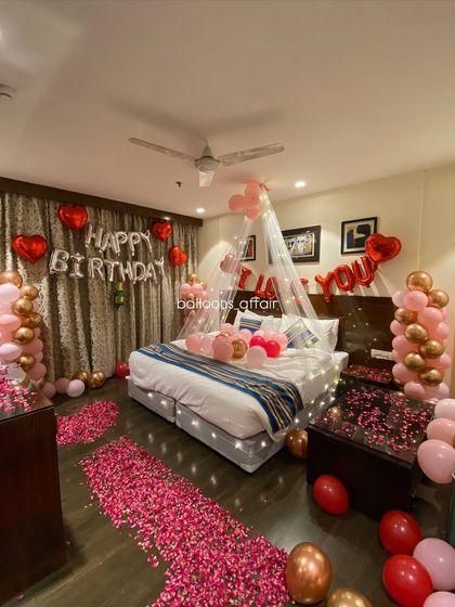 A full room view showing the balance of balloon columns, floor petals, and bed decorations in this rose gold themed birthday surprise.