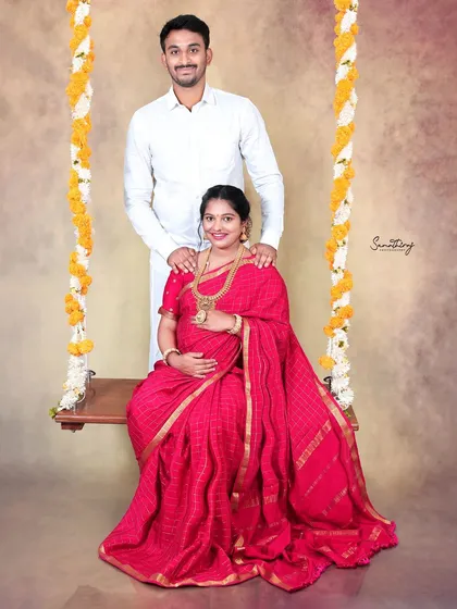 A playful and sweet moment captured on a swing decorated with flowers. The vibrant red saree adds a pop of color, making this a joyful and memorable traditional portrait.