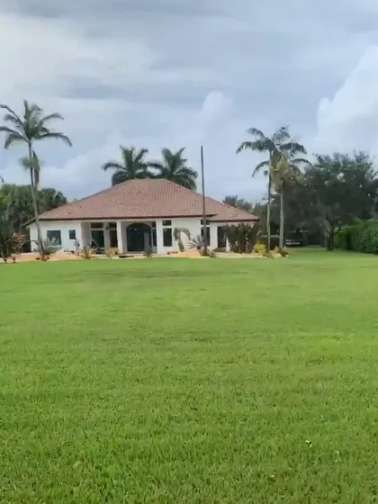 The completed exterior of a modern farmhouse. The design features a tiled roof, large arched entryways, and an expansive lawn, creating a serene and impressive property.