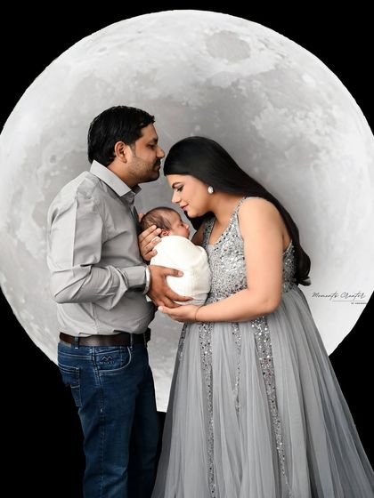 A creative family portrait with a full moon backdrop. The parents hold their newborn, creating a magical and memorable "to the moon and back" themed photo.