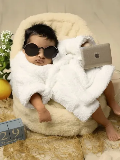 This little boss is already taking meetings. A fun and humorous newborn setup featuring a tiny bathrobe, sunglasses, and a laptop, proving that even the tiniest clients can have a big personality.