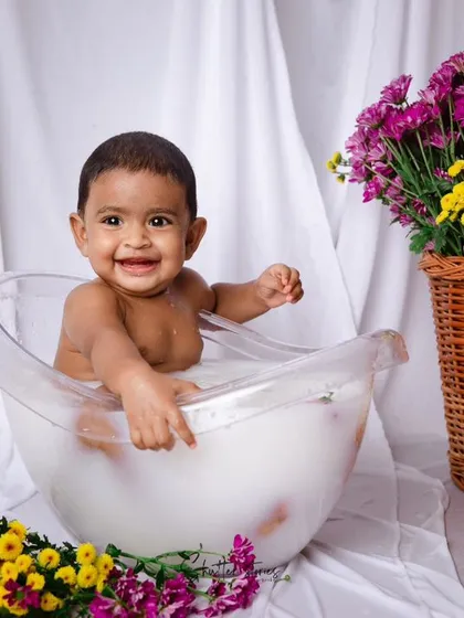 A happy baby enjoying her milk bath, surrounded by colorful flowers.