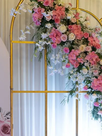 A close-up of the lush floral arrangement cascading down the golden arch backdrop, featuring a mix of pink and white roses and orchids.