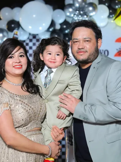 A formal family portrait from a second birthday party. The family is dressed elegantly in front of the party decorations.