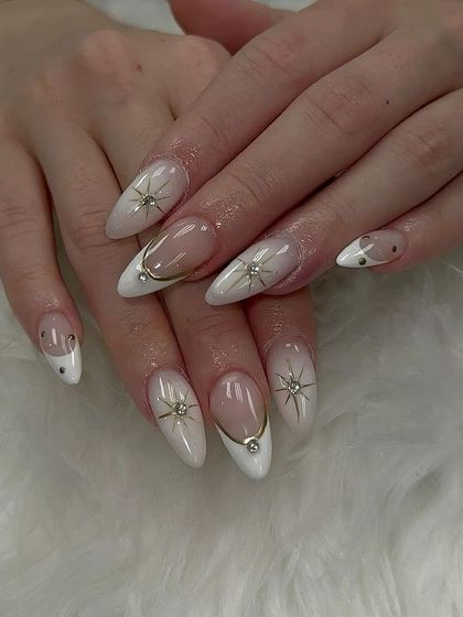 A celestial-themed design with a milky white base, gold-lined French tips, and delicate starbursts with rhinestone centers.