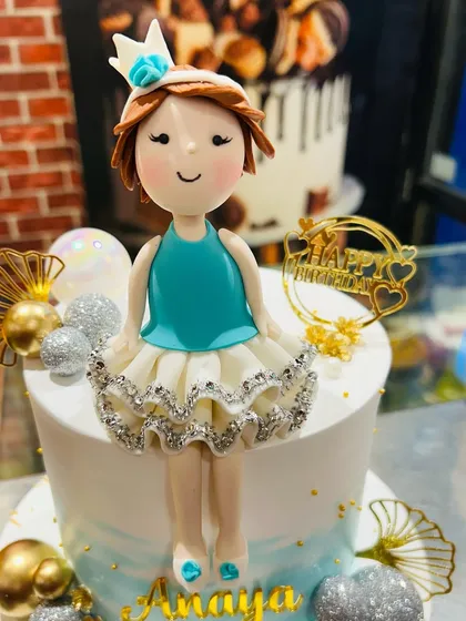 A close-up of a beautifully crafted fondant doll topper with a sparkly silver dress.