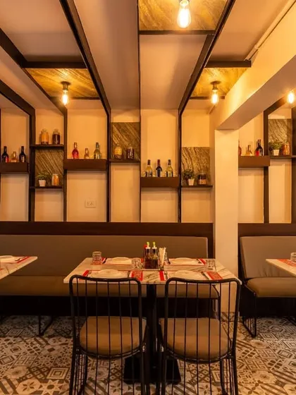 A cozy dining nook designed with long booth seating against a wall featuring decorative shelving and vertical wood-finished panels. The exposed Edison bulbs hanging from the ceiling add a warm, vintage touch to this intimate area.