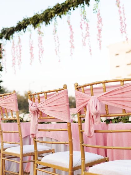 A close-up of the chair decor, with delicate pink fabric tied in a knot on golden chiavari chairs.