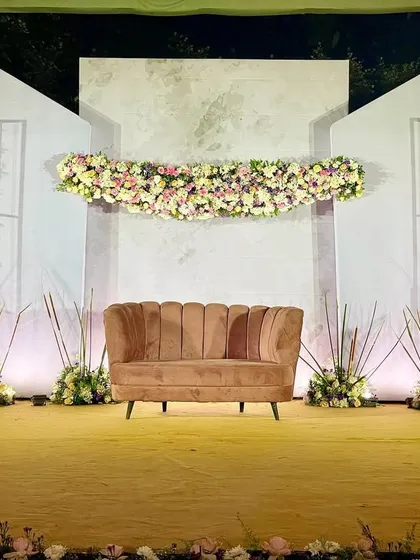 A chic and modern stage design featuring clean, angular white panels, vertical floral arrangements, and a stylish brown sofa as the centerpiece.