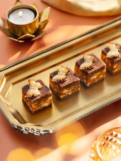 These unique sweets, topped with butterfly-shaped crisps, were part of the Marriott Diwali shoot. The warm, glowing light from the diya in the background adds a traditional and auspicious touch to the modern presentation.