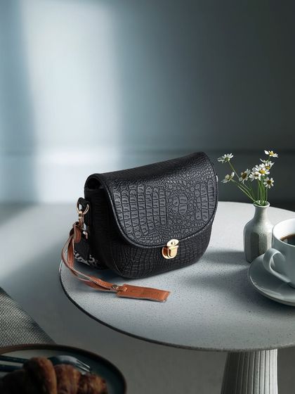 A lifestyle shot of a black crocodile-texture bag on a cafe table with a cup of coffee. This places the product in a chic, everyday context.