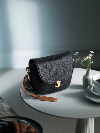 A lifestyle shot of a black crocodile-texture bag on a cafe table with a cup of coffee. This places the product in a chic, everyday context.