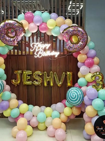 A sweet candy-themed birthday decoration. This balloon ring is decorated with pastel colors, donut foil balloons, and a "Happy Birthday" neon sign, with the name in gold foil letters.