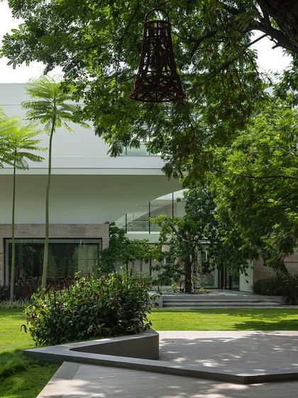 A view of a modern white house with clean lines and large glass windows. The landscape in the foreground features tall palm trees and a manicured lawn, creating a stark, beautiful contrast between the built and natural forms.
