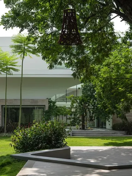 A view of a modern white house with clean lines and large glass windows. The landscape in the foreground features tall palm trees and a manicured lawn, creating a stark, beautiful contrast between the built and natural forms.