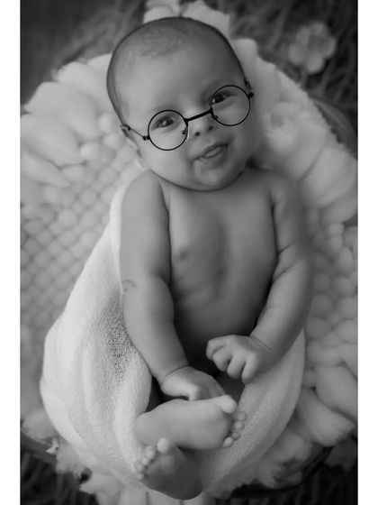 The same playful shot with glasses, presented in classic black and white. This version highlights the baby's adorable expression and the simple, charming prop without the distraction of color.
