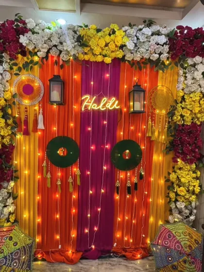 A festive Haldi backdrop with a mix of colorful drapes, a bright neon sign, and traditional decor elements. The combination of flowers, lights, and lanterns makes it a perfect spot for photos.