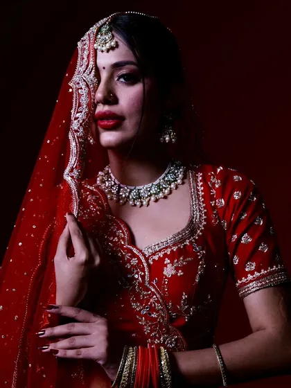 A direct and powerful bridal portrait. The bride looks straight at the camera, her expression confident, with the rich red of her lehenga creating a bold statement.