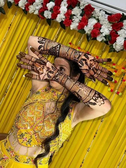 A happy bride posing with her full figurative bridal mehandi, which covers her hands and arms in beautiful stories and patterns.