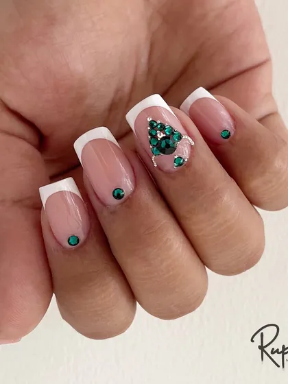 A classic French manicure gets an upgrade with a stunning emerald green Swarovski crystal tree design. This is a perfect example of festive or holiday nail art.