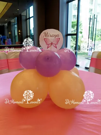 A simple table centerpiece with purple and peach balloons and a custom "Miraya" sign with a butterfly motif.