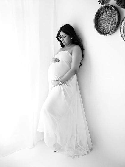A solo portrait of a mumma-to-be, draped in white fabric. The black and white edit gives it a soft, ethereal quality, highlighting the gentle curves of pregnancy.