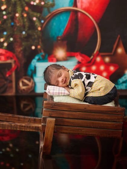 Inspired by Toy Story, this little cowboy in a cow-print shirt sleeps on a wooden cart with a festive, toy-filled background.