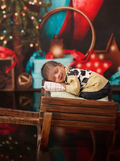 Inspired by Toy Story, this little cowboy in a cow-print shirt sleeps on a wooden cart with a festive, toy-filled background.