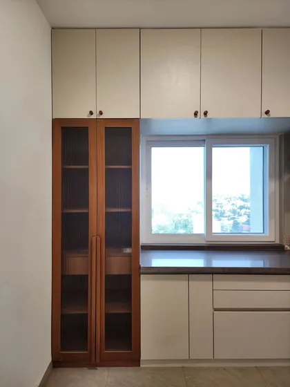 A kitchen storage unit designed to maximize space and light. The tall, glass-fronted cabinet provides elegant display storage, while the large window brings in ample daylight, making the kitchen feel bright and airy.