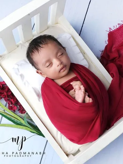 The baby is now resting peacefully in the bed, swaddled in red.