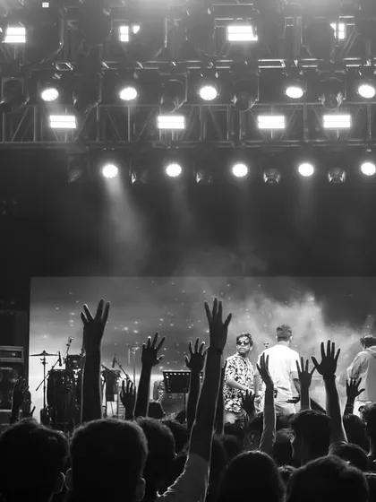 A black and white perspective from the back of the venue, focusing on the audience's participation with hands raised in the air, creating a powerful, timeless concert image.