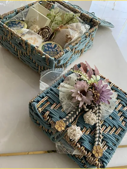 A view of the closed blue jute hamper, highlighting the intricate weaving and the beautiful floral and rope embellishments on the lid.