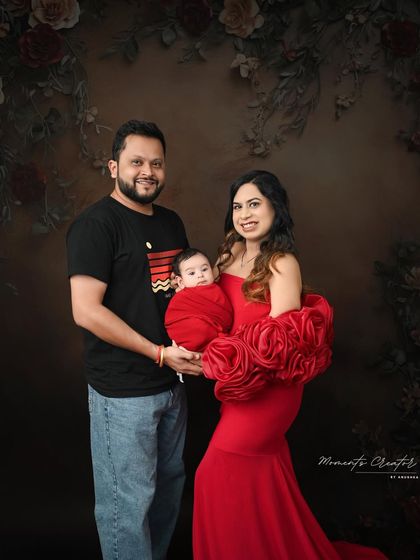 A vibrant family portrait with a newborn. The mother's stunning red dress with rose details complements the baby's red swaddle, creating a bold and beautiful image.