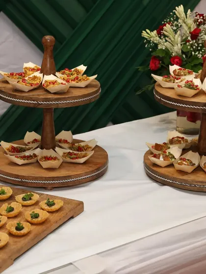 An elegant corporate event setup featuring tiered stands with savory canapés. The clean white and green theme creates a professional yet welcoming atmosphere.