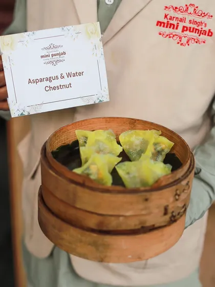 Our Asparagus and Water Chestnut Dimsum, presented by a server in a bamboo steamer. These vegetarian dumplings are a light, healthy, and delicious option.