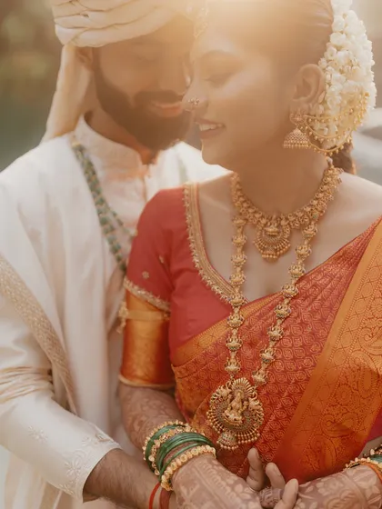 A sun-kissed, romantic close-up of a South Indian couple, focusing on the bride's stunning temple jewelry.