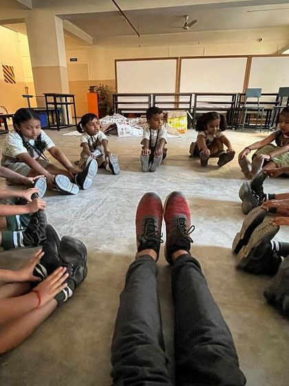 A flexibility game where children sit in a circle and try to touch their toes. This instructor's-eye-view shows how we make stretching interactive and fun for everyone.