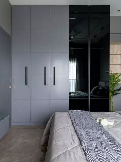 Elegance meets functionality in this modern minimalist bedroom design. The sleek grey wardrobes with reflective finishes complement the textured wall and glass accents, creating a harmonious balance of sophistication and utility.