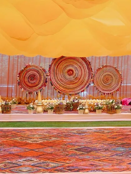 The dance floor and stage for the equestrian Haldi, featuring a rustic printed rug and a backdrop of woven textures, all under a canopy of wavy orange fabric.