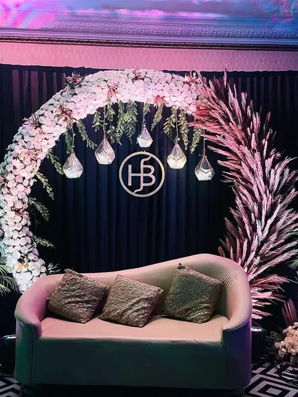 This special seating area for a Sangeet combines a floral and pampas grass arch with a custom logo. The dark backdrop makes the white flowers and lighting pop, creating a modern and moody vibe.
