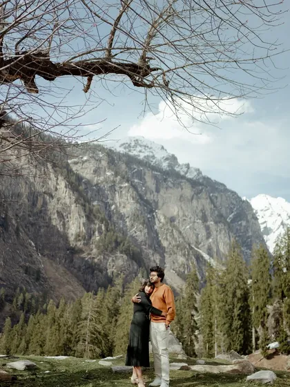 A beautiful portrait of a couple framed by the mountains in Manali. The bare branches of the tree add a rustic, artistic element to this romantic landscape shot.