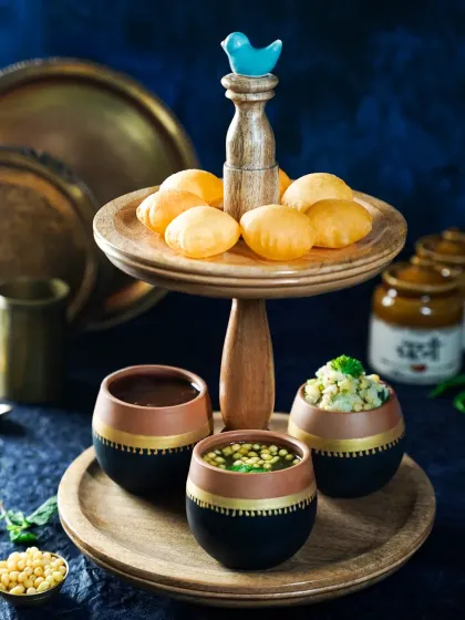 A creative presentation of Pani Puri, with the puris on a wooden tier stand and the flavored waters in stylish terracotta pots. This modern twist on a classic street food dish is both elegant and playful.
